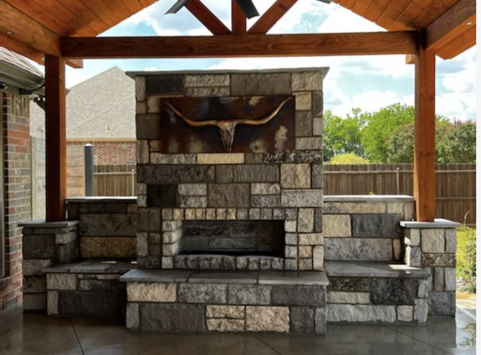 Stone outdoor fireplace with longhorn art under a cedar pavilion