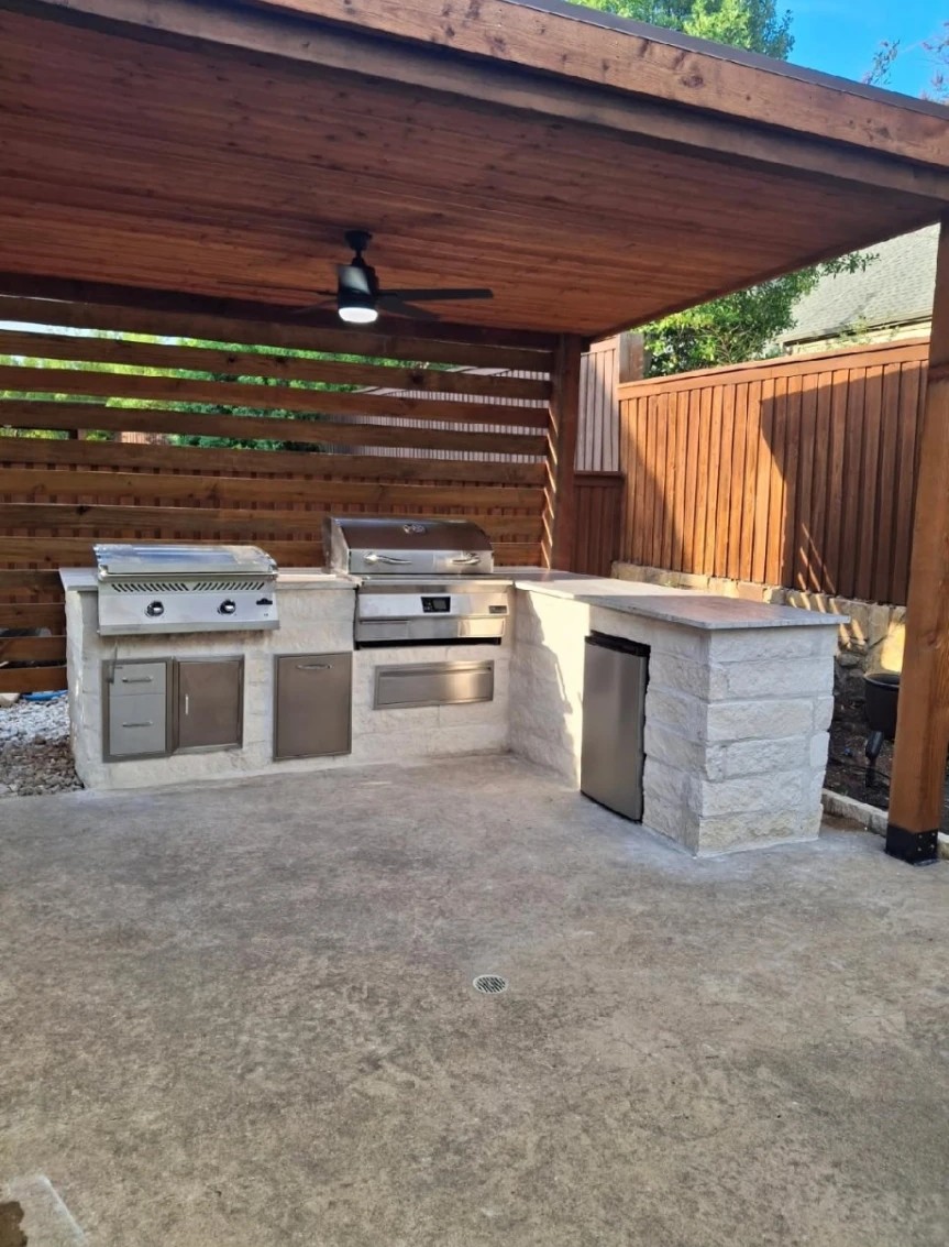 White limestone L-shaped outdoor kitchen with cedar privacy screen