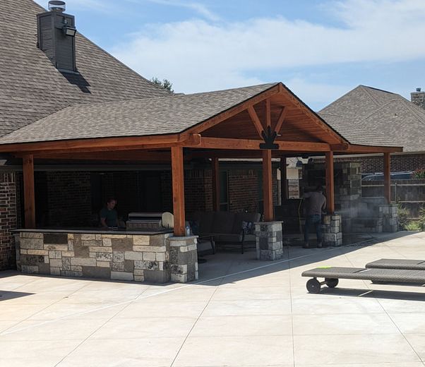 Covered cedar pavilion with stone grill island beside a Texas home